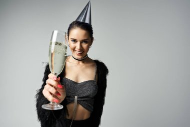Young woman in party hat, holding champagne glass, exuding joy and style in studio setting.