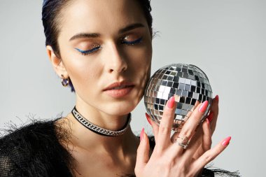 Stylish young woman with short dyed hair holding sparkling disco ball, exuding joy and celebration vibes.