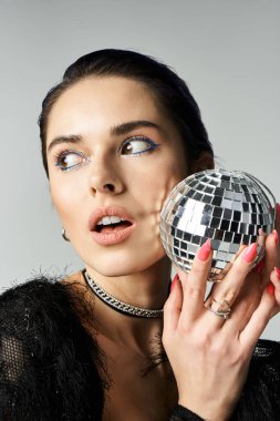 Young woman with short dyed hair holds a disco ball up to her face, exuding fun and glamour in a stylish studio setting.