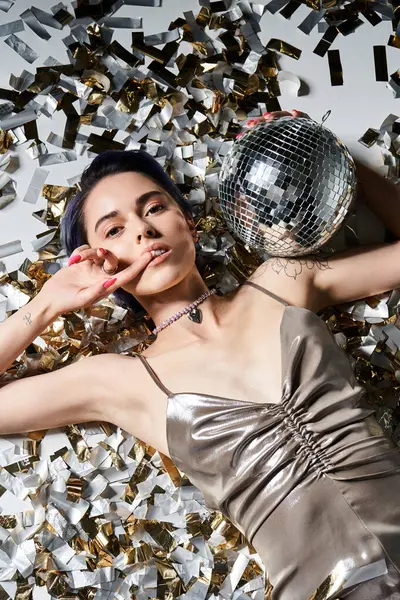 stock image A young woman with short blue hair striking a pose in a shimmering silver party dress, holding a sparkling disco ball.