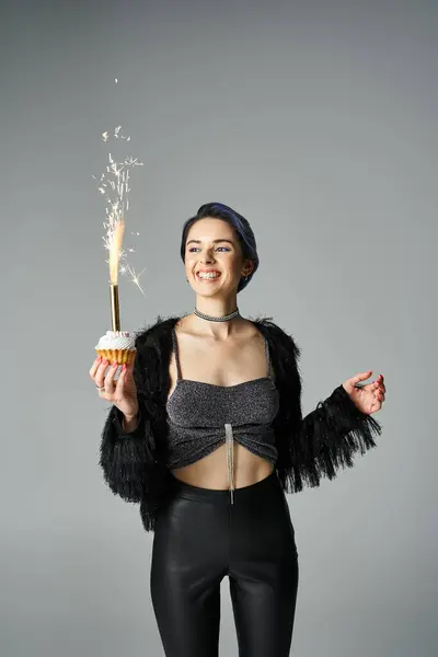 stock image A young woman joyfully holding a cupcake with a sparkler, celebrating a birthday in a stylish setting.