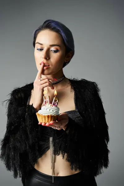 stock image A young woman with short dyed hair poses in a black jacket, holding a delicious cupcake.