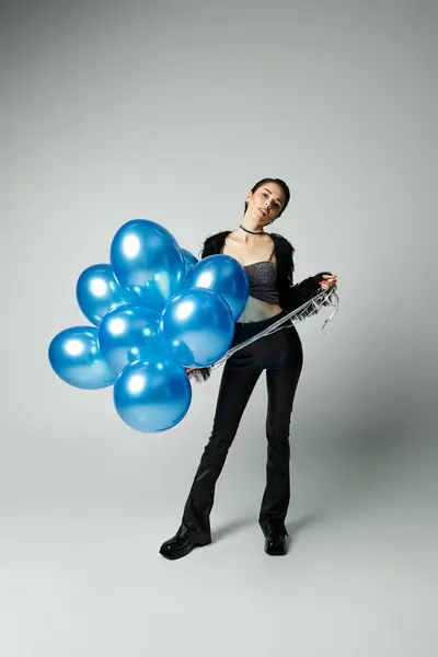 stock image A vibrant young lady with chic style clutches a bunch of radiant blue balloons.