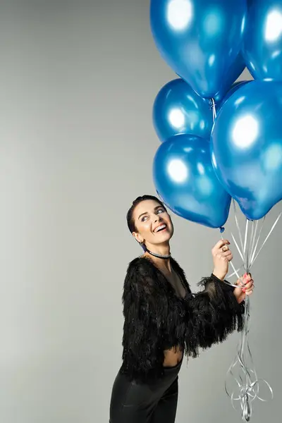 stock image A young woman with short dyed hair dressed stylishly holding a bunch of blue balloons in a studio setting.