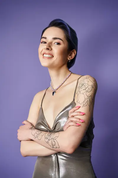 stock image A young woman with blue hair strikes a pose in a stunning silver dress, showcasing intricate tattoos on her arms.