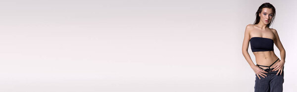 Young, wet-haired woman in a black bikini stands against a white wall.