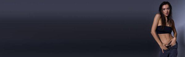 A young, alluring woman with wet hair standing confidently in front of a gray backdrop.