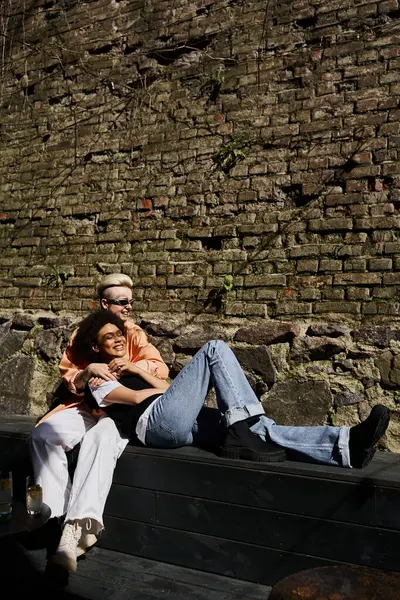 Stock image Two women sitting together on a bench in front of a stone wall.