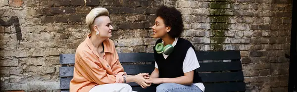 stock image A diverse couple of lesbians sit peacefully on a bench near a brick wall.