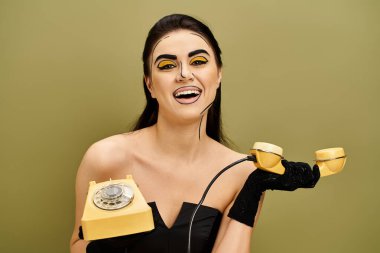 Siyah elbiseli ve eldivenli şık esmer, elinde parlak sarı bir telefon tutarken klasik cazibeyi somutlaştırıyor..