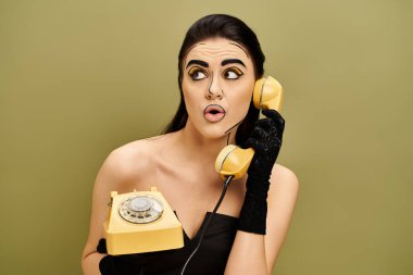 A fashionable brunette woman in a black dress and gloves, holding a yellow retro telephone. clipart