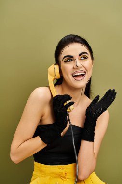 Göz kamaştırıcı esmer bir kadın, pop-art makyajlı, siyah bir bluz giymiş, telefondan kulağa ayakta duran.