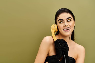 Sarı telefonlu, siyah elbiseli kadın, pop sanat makyajı ve siyah eldivenleri sergiliyor..