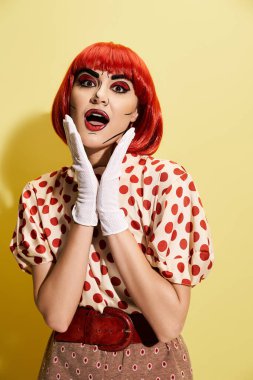 Popüler sanat makyajlı çarpıcı kızıl saçlı bir kadın koyu sarı bir zemine karşı puantiyeli gömlek ve beyaz eldivenler giyer..