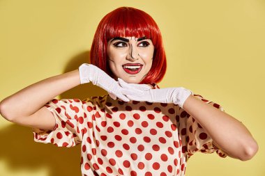 Göz kamaştırıcı kızıl saçlı bir kadın, parlak sarı bir arka plana polka noktalı bir tişört giyip bir çizgi romandaki karakteri somutlaştırıyor..