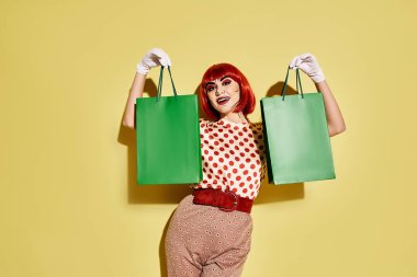Popüler sanat makyajlı şık bir kızıl saçlı kadın ve parlak sarı arka planda alışveriş torbaları tutan benekli bluz..