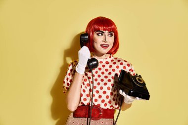 Canlı bir kızıl saçlı, pop sanatları makyajı ve puantiyeli bluzuyla kalın sarı arka planda bir telefon tutuyor..
