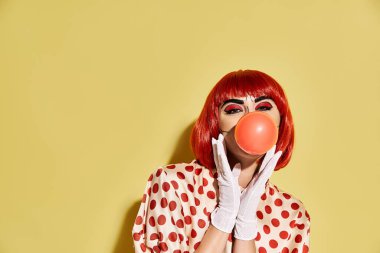 Popüler sanat makyajlı güzel bir kızıl kadın, sarı arka planda balon şişiriyor..
