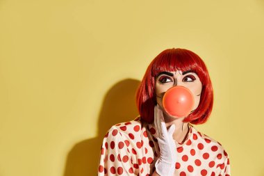 Canlı kızıl saçlı, yaratıcı pop sanat makyajlı, benekli bluzlu balon şişiren bir kadın.