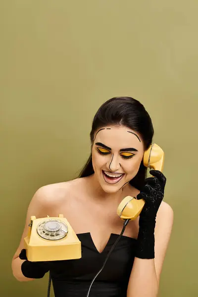 stock image Stylish brunette in black dress and gloves holds yellow phone, embodying retro glamour with pop art makeup.