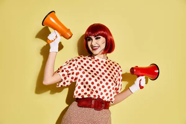 stock image Creative redhead woman with pop art makeup in a polka dot shirt, holding a red and orange megaphone on a yellow backdrop.