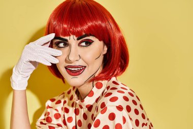 Benekli tişörtlü, beyaz eldivenli, yaratıcı pop sanat makyajlı güzel bir kızıl kadın sarı arka planda duruyor..
