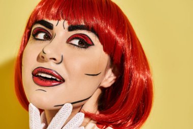 Kırmızı saçlı, yaratıcı pop sanat makyajlı, puantiyeli bluz giymiş, sarı arka planda oturan güzel bir kızın yakın çekimi..