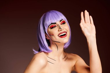 Mor saçlı ve pop sanat makyajlı çarpıcı bir kadın elini kaldırıyor, çizgi romandaki bir karakteri somutlaştırıyor..