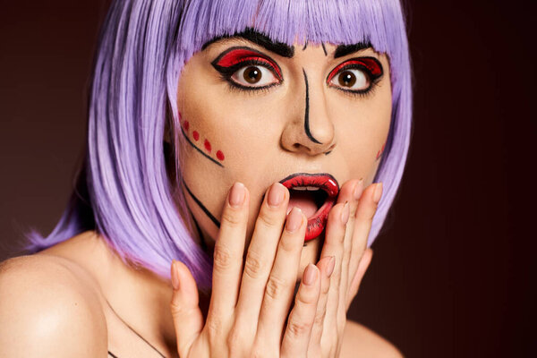 Женщина с фиолетовыми волосами и поп-арт макияж задыхается, руки закрывают рот в благоговении.
