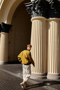 Young red-haired man stands confidently in front of a sleek building. clipart