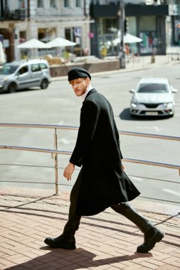 Uzun siyah ceketli, kızıl saçlı genç bir adam şehir caddesinde yürüyor..