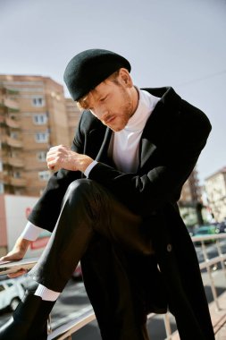 A red-haired man in debonair attire and a hat sitting gracefully on a ledge in the city. clipart