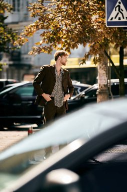 Young red-haired man in debonair attire casually walking down a city street lined with parked cars. clipart