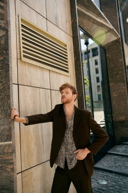 Şık takım elbiseli kızıl saçlı adam şehir duvarına yaslanıyor..