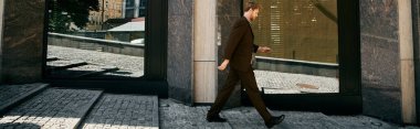 A fashionable young red-haired man in a suit confidently walks down a city sidewalk. clipart