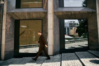 Genç kızıl saçlı, güler yüzlü bir adam şehrin yüksek bir binasının önünden geçiyor..