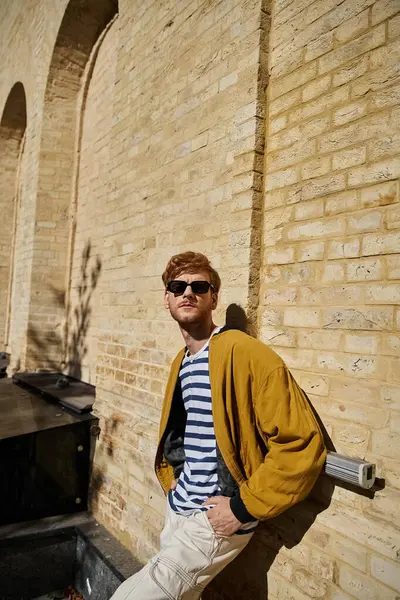 stock image Stylish young man with red hair standing confidently in front of brick wall.