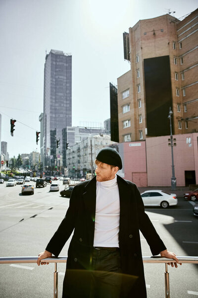 Стильный рыжий мужчина в городском шикарном ансамбле небрежно опирается на уличные рельсы..