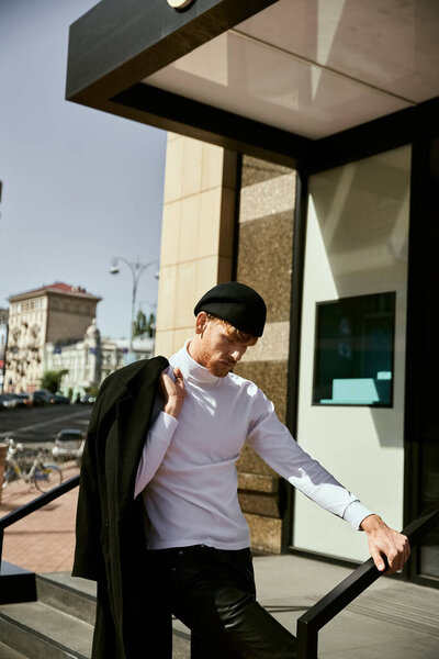 Молодой рыжий мужчина излучает элегантность в белой рубашке и черных штанах во время прогулки по городу.