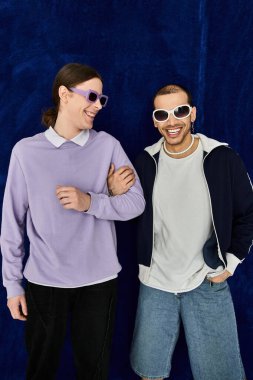 İki adam, canlı mavi bir arkaplanda yan yana durur..