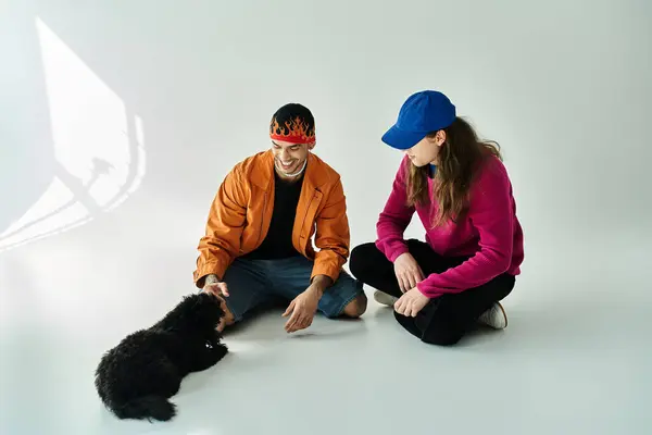 stock image two men sit beside a black dog, sharing a peaceful moment.