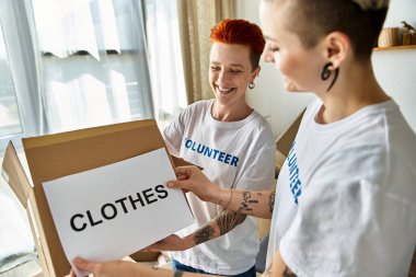 Two women in volunteer t-shirts standing together with pride and unity as they work on a charity project. clipart