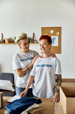 Two women in volunteer t-shirts standing united in a room, working together for a cause they believe in. clipart