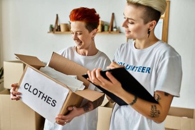 Young lesbian couple in volunteer t-shirts collect donation boxes for charity work. clipart