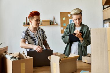 Young lesbian couple organizing boxes in a room, working together for charity. clipart