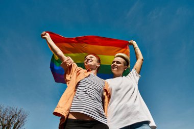 Genç lezbiyen bir çift dışarıda gökkuşağı bayrağı tutarak LGBTQ toplumunda sevgi ve gurur ifade ediyorlar..