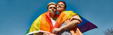 A young lesbian couple, holding a rainbow flag, sharing a warm hug in a celebration of love and LGBTQ pride. clipart