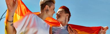 Dışarıda gökkuşağı bayrağı taşıyan genç bir çift LGBTQ topluluğuna destek veriyor..