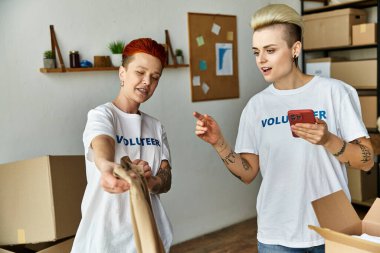 A young lesbian couple in volunteer t-shirts actively participating in charity work together. clipart