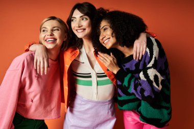 A group of young, beautiful women in vibrant clothes of different cultures standing together on an orange background. clipart